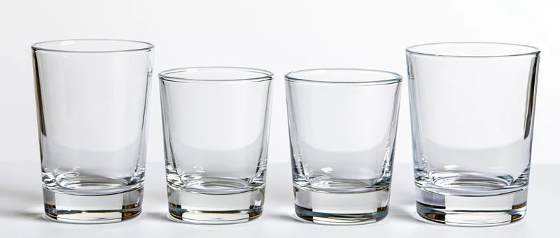 Four empty clear drinking glasses arranged in a row on a white surface