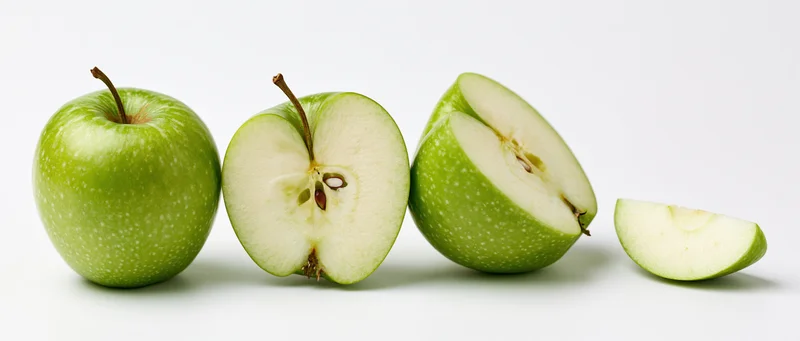 Four green granny smith apples arranged in a row, whole and sliced, on a white background