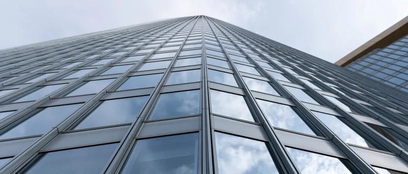 Low angle view of a modern corporate skyscraper's glass curtain wall reflecting sky and clouds