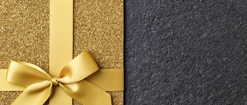 Gold satin ribbon tied in a bow on glittery surface beside dark textured background