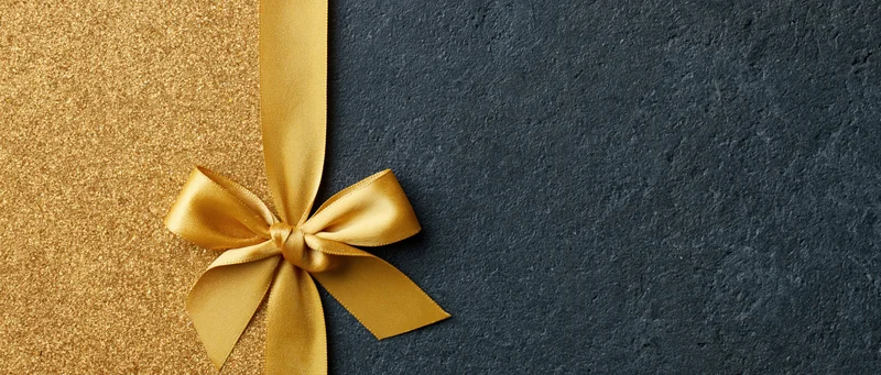 Gold satin ribbon tied in a bow on a dark textured surface with copyspace