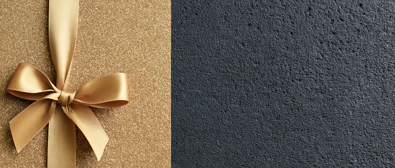 Gold satin ribbon tied in a bow on a glittery surface next to a dark textured background