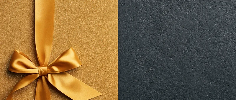 Gold satin ribbon tied in a bow on a glittery surface beside a dark textured background