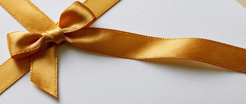Gold satin ribbon tied in a small bow on a white gift box surface