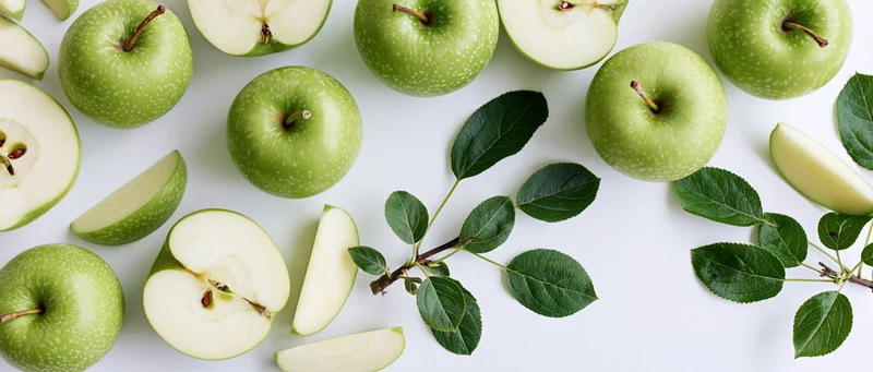 Green apples whole and sliced with leaves arranged in flat lay on white background