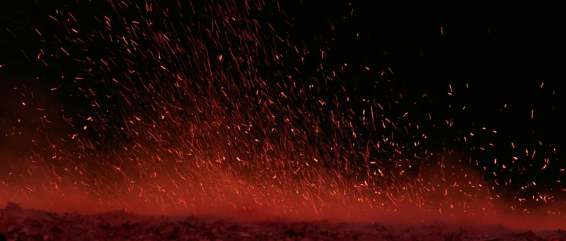 Glowing red sparks rising upward from a dark ground at night