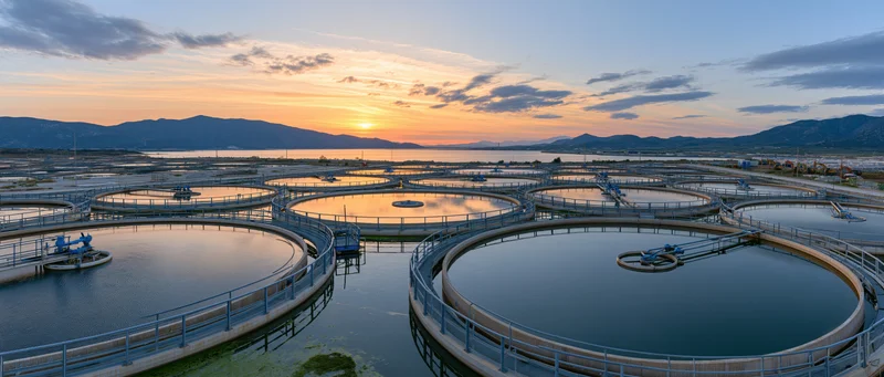 Circular water tanks at a large aquaculture fish farm during sunset with mountains in the background