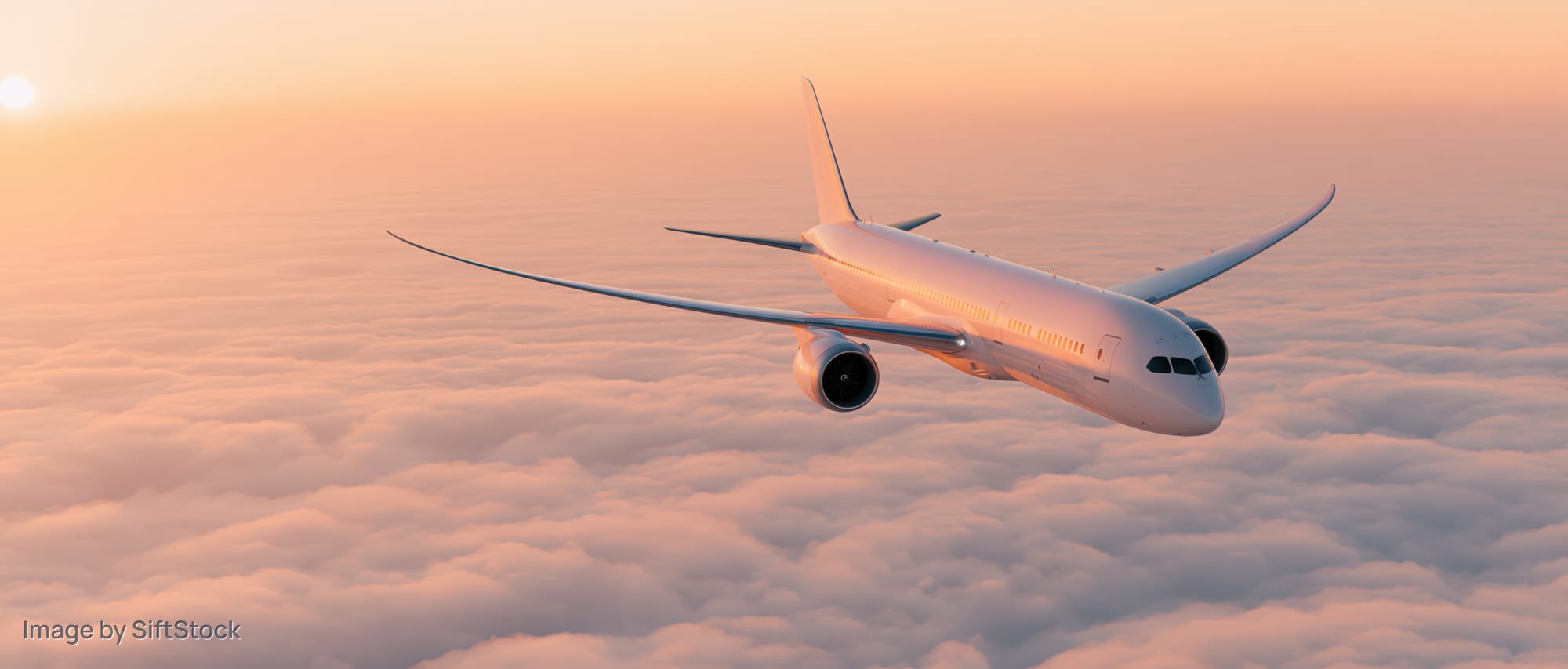 Commercial passenger jet cruising above a thick blanket of clouds at sunset