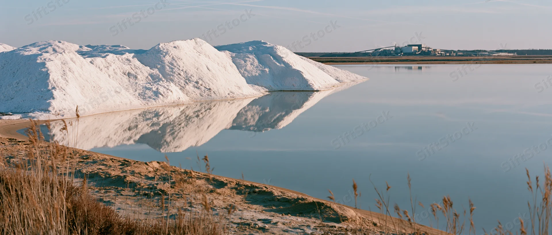 Large white salt piles reflected in calm water at an industrial salt flat