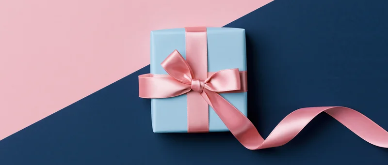 Light blue gift box tied with pink satin ribbon and bow on pink and navy background