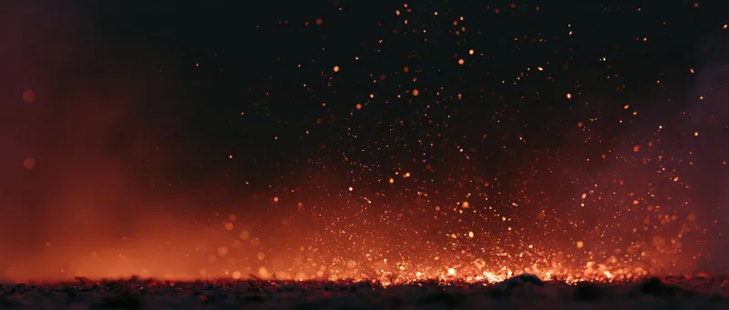 Flying sparks and glowing embers rising from a fiery base against a dark background