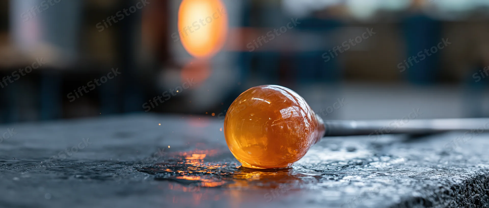 Molten glass globe on a blowpipe resting on a wet metal surface in a workshop