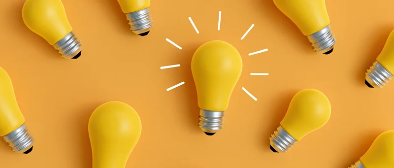 Yellow lightbulbs scattered in flat lay on orange surface with one glowing in center