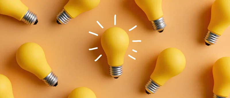 Yellow light bulbs arranged in scattered flat lay on orange surface