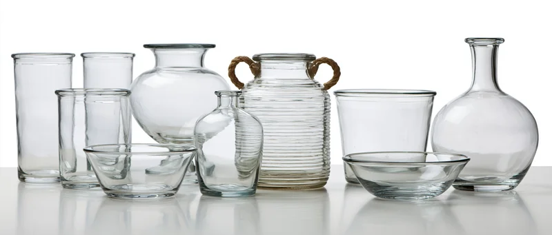 Nine empty clear glass vessels arranged in a row on a reflective white surface