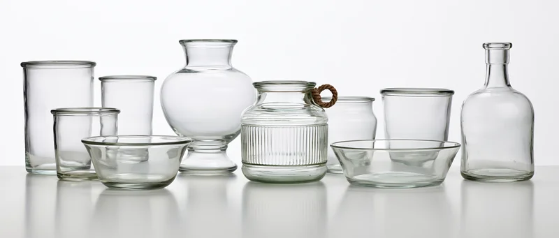 Nine empty clear glass vessels arranged in a row on a white reflective surface