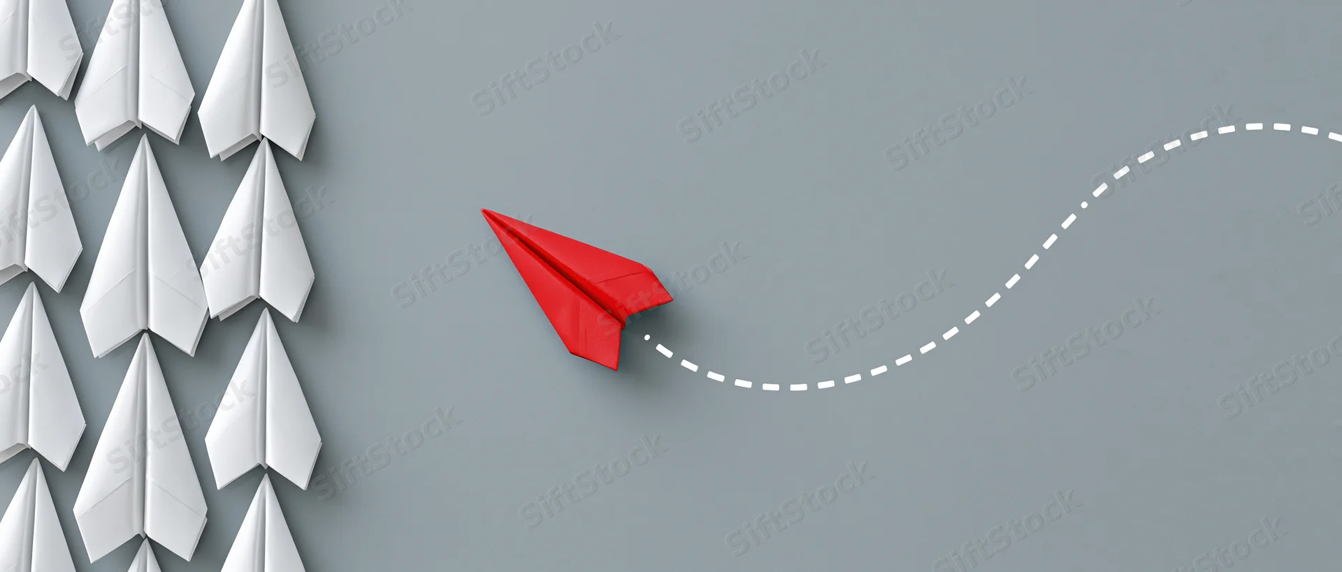 Red paper airplane breaking away from a group of white ones on gray background