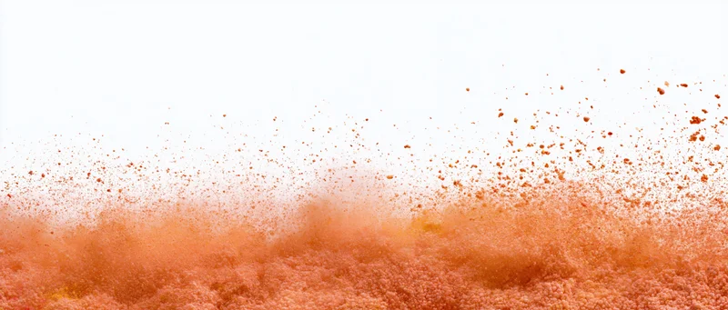 Orange and red powder exploding mid-burst in a dynamic cloud of airborne particles