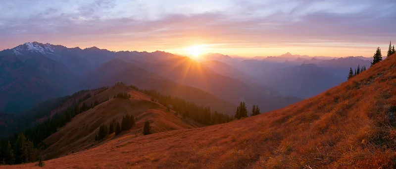 Panoramic alpine landscape at golden sunset with layered mountains and forested slopes