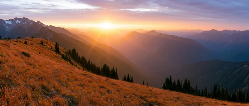 Panoramic alpine landscape at golden sunset with layered mountains and grassy slopes