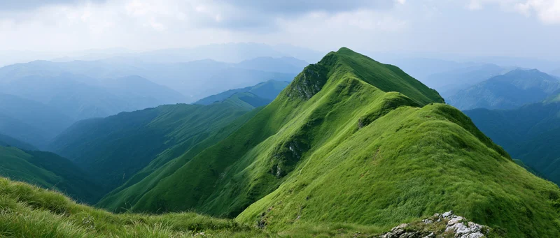 Layered green mountain ridges receding into the distance under a cloudy sky