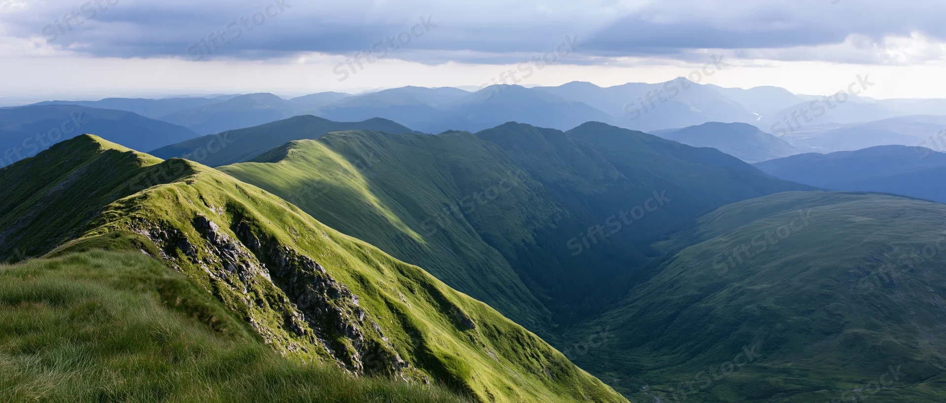 Panoramic view of layered green mountain ridges receding into the distance under a cloudy sky