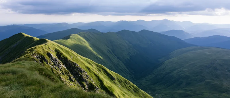 Panoramic view of layered green mountain ridges receding into the distance under a cloudy sky