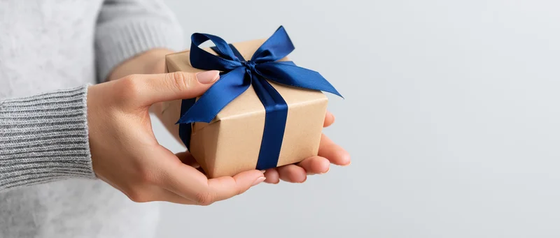 Woman holding small kraft paper gift box tied with blue ribbon against white background