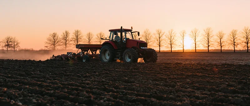 Red tractor pulling tillage equipment across a plowed field at sunset