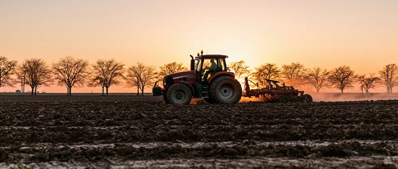 Red tractor pulling tillage equipment across a plowed field at sunset