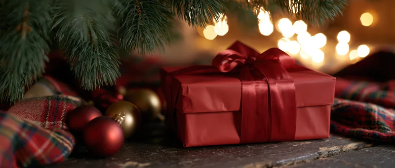 Red gift box with satin bow under christmas tree on wooden floor
