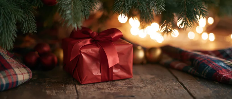 Red gift box with satin bow under christmas tree on wooden floor