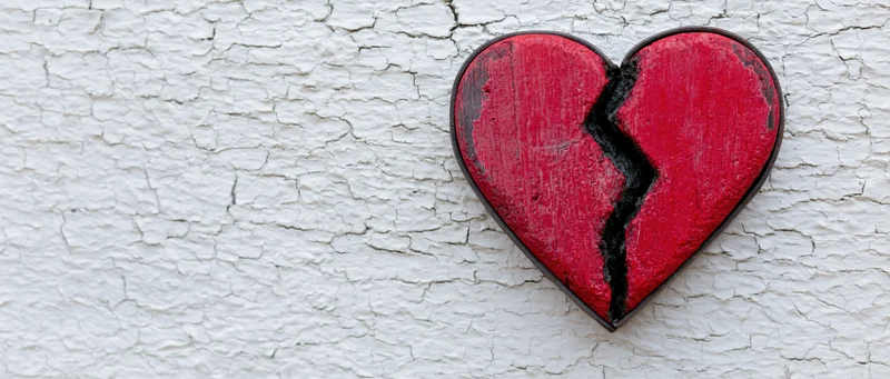 Red painted wooden broken heart mounted on a cracked white wall