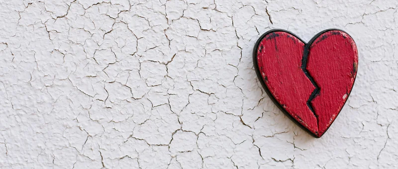 Broken red wooden heart mounted on a cracked white wall