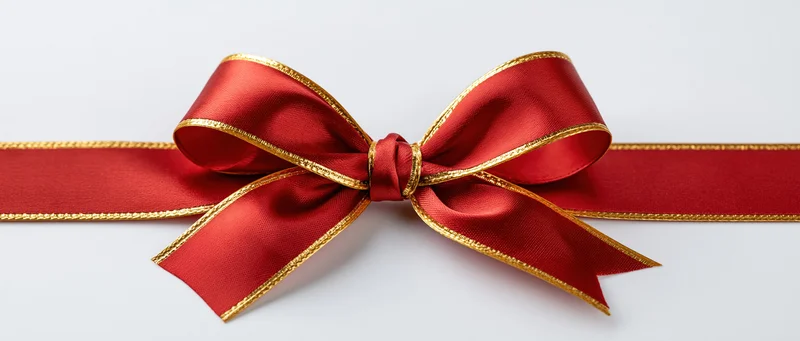 Red satin ribbon with gold trim tied into a bow on a white background
