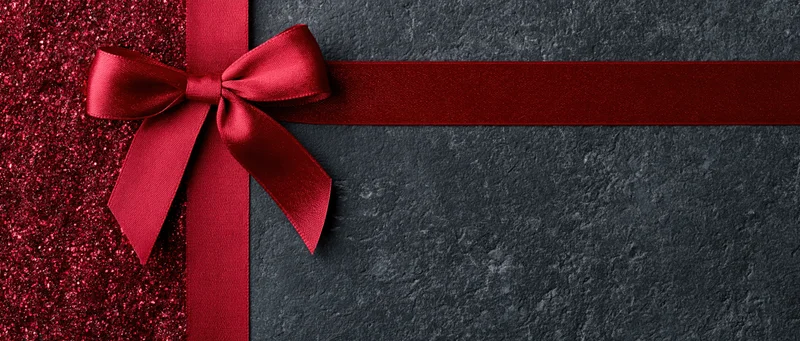 Red satin ribbon tied in bow across dark textured surface with glittery red side panel