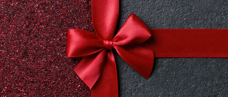 Red satin ribbon tied in a bow across a dark textured banner with glittery red side panel