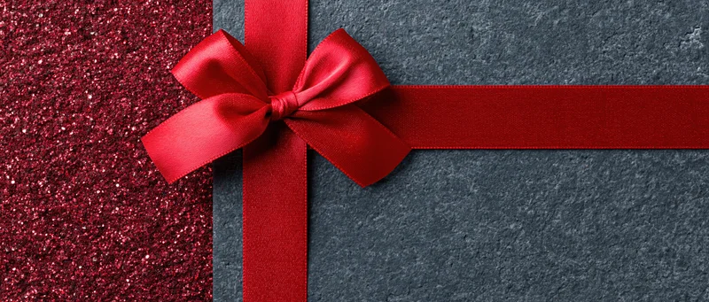 Red satin ribbon tied in bow across wide banner with glitter and dark textured surface