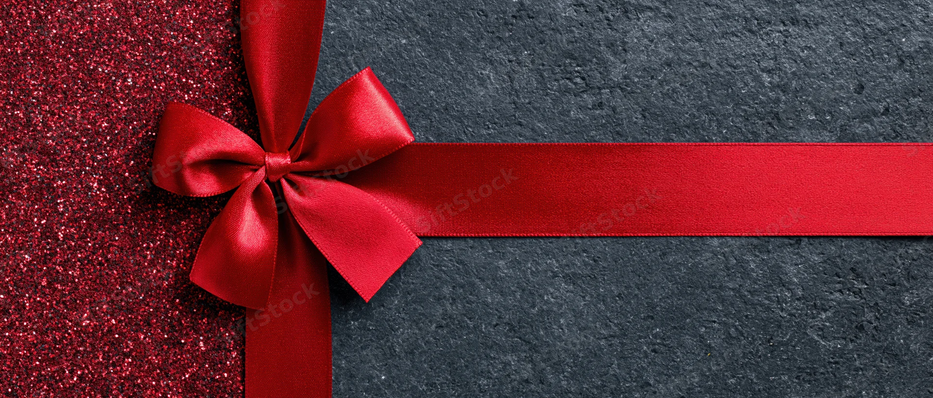 Red satin ribbon tied in bow across dark textured surface with glittery red section on left