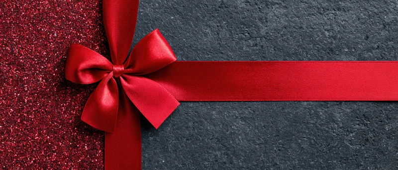 Red satin ribbon tied in bow across dark textured surface with glittery red section on left