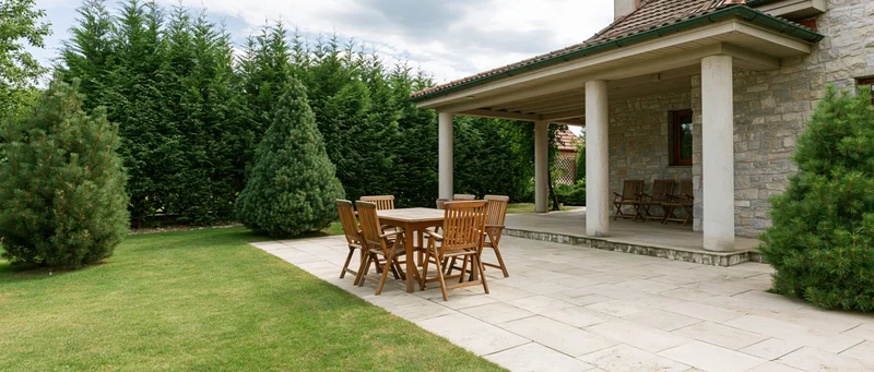 Residential backyard with patio and wooden furniture surrounded by manicured lawn and ornamental conifers