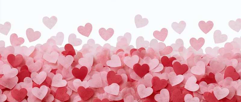 Scattered pink and red paper heart confetti pieces covering a white surface with copyspace at the top