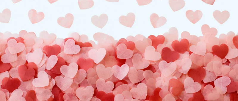 Scattered pink and red paper heart confetti forming a textured pile against a white background with copyspace above