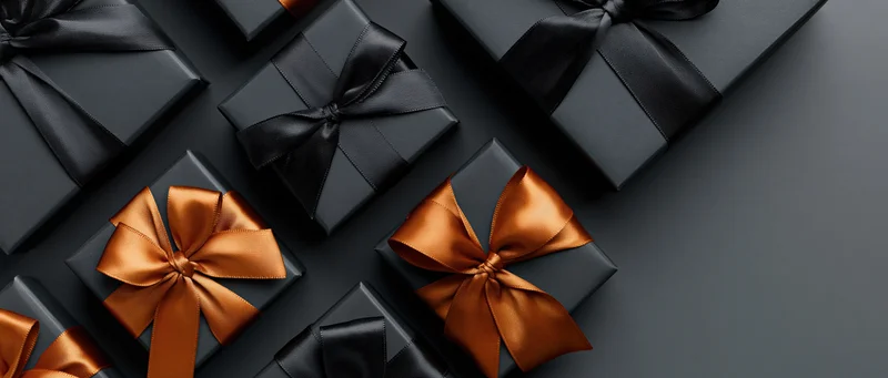 Matte black gift boxes wrapped with black and copper satin ribbons arranged on dark surface