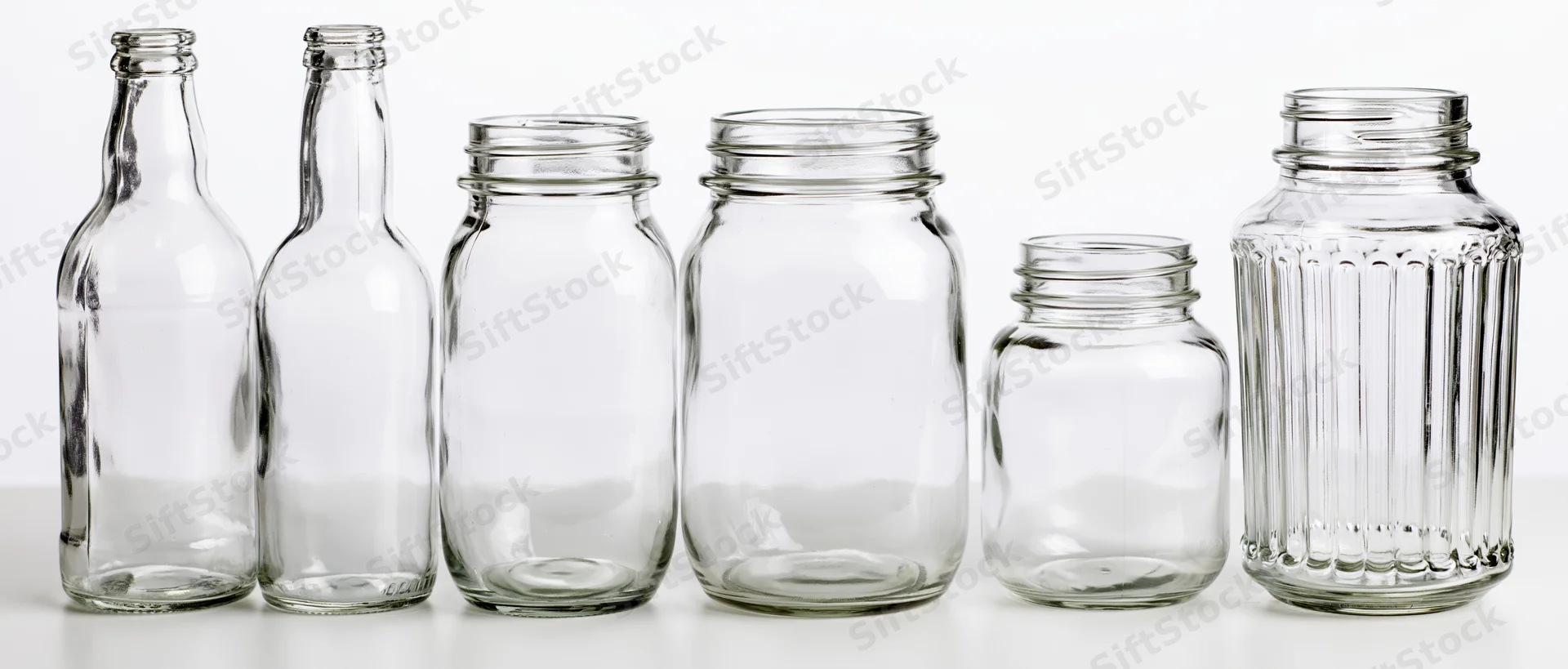 Six empty clear glass bottles and jars arranged in a row on a white surface
