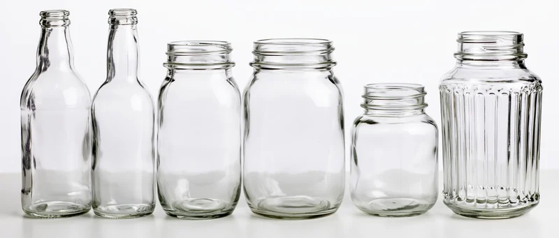 Six empty clear glass bottles and jars arranged in a row on a white surface