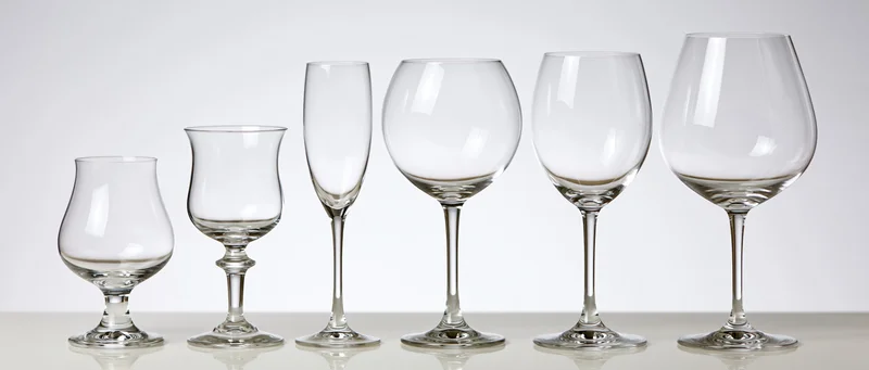 Six empty glassware pieces arranged in a row from shortest to tallest on a white surface