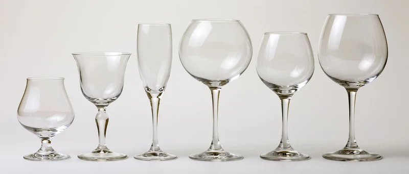 Six empty glassware pieces arranged in a row from shortest to tallest on a white surface