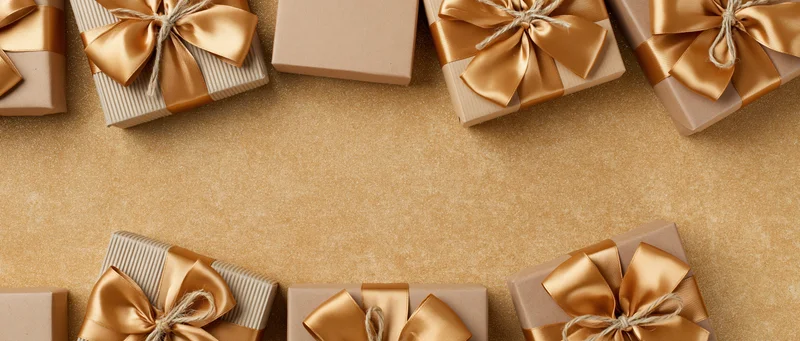 Gift boxes with gold satin bows arranged on a textured gold surface with copyspace in the center