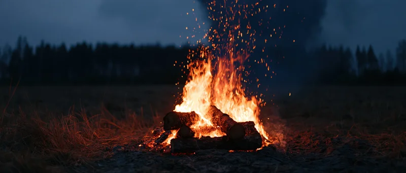 Campfire burning with stacked logs in a field at night